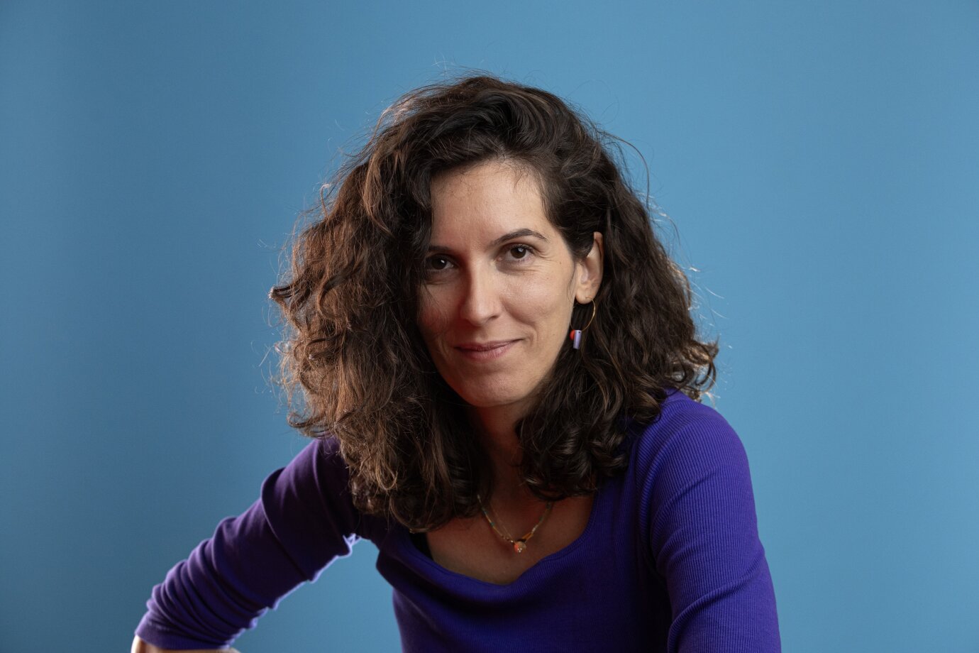 Porträt von Svetlana Maraš vor blauem Hintergrund: eine ca. 40jährige, schlanke Frau mit schulterlangen, gelockten braunen Haaren.