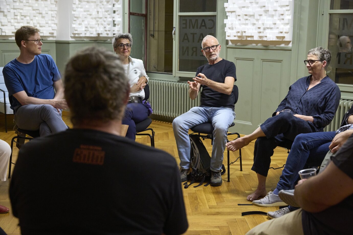 Ein ca. 10köpfige Gruppe erwachsener Personen sitzt auf Stühlen im Kreis und unterhält sich aufmerksam. 