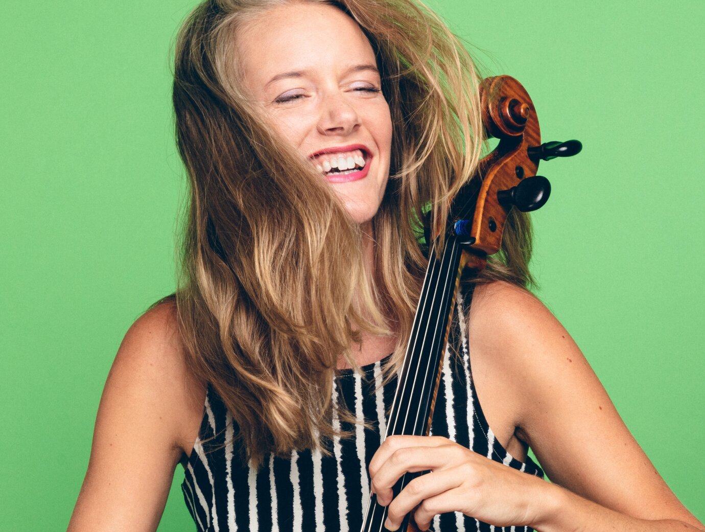 Die Cellistin Karolina Öhmann spielt freudvoll auf ihrem Instrument. Das Bild strahlt durch seinen hellgrünen Hintergrund. 